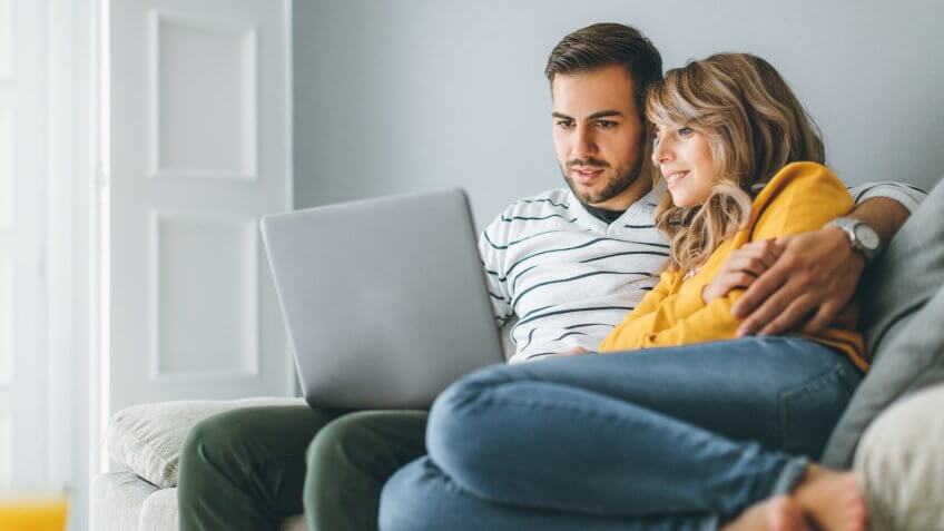 Young cheerful couple using laptop at home.