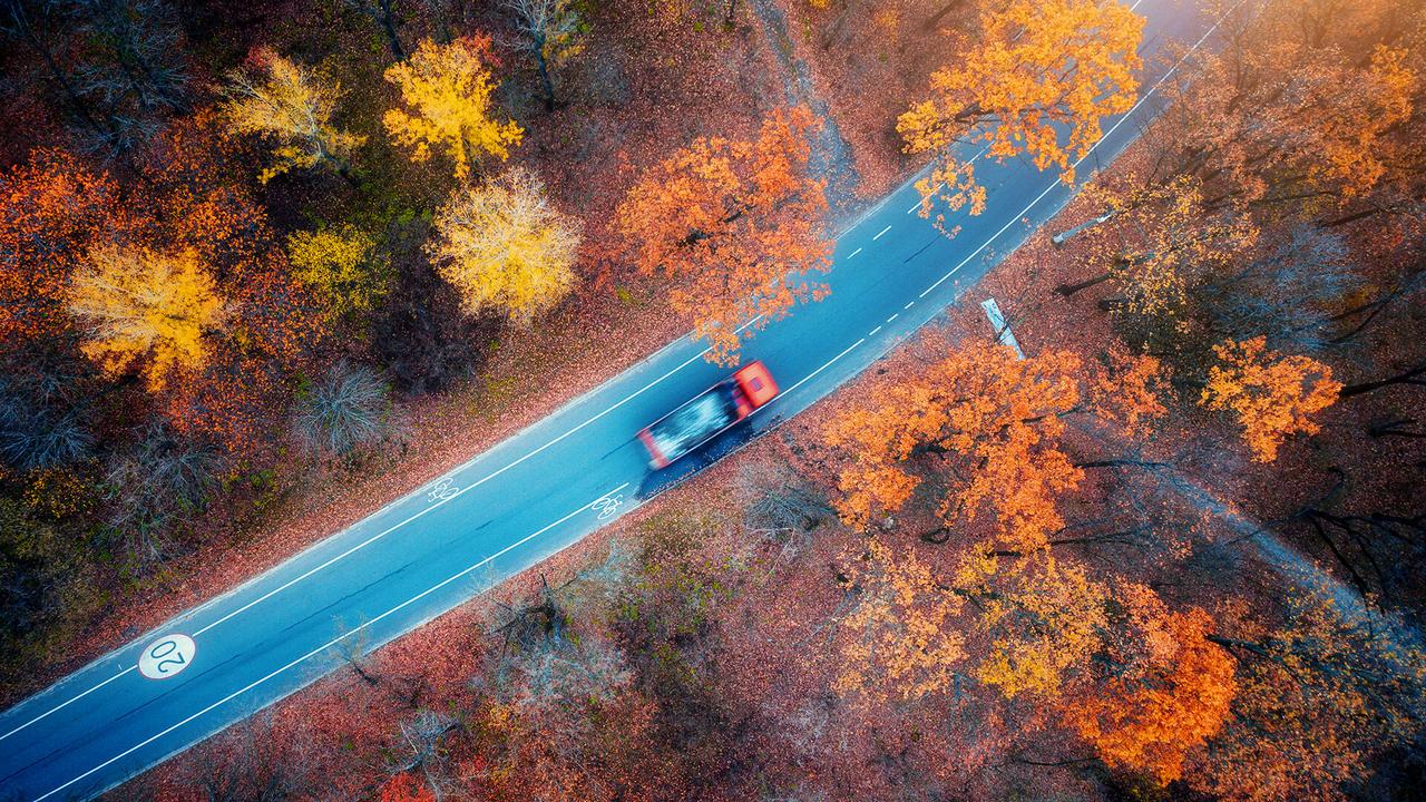 Aerial view of road with blurred car in autumn forest at sunset.