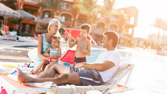 Happy mid adult parents enjoying with their little children at the poolside during summer day.