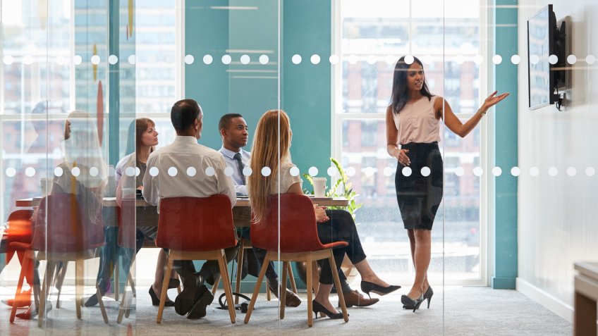 Female boss shows presentation on screen at business meeting.