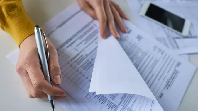Close-up of unrecognizable woman attentively examining business documents and making correction at table.