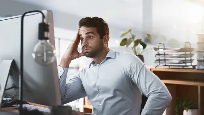 Shot of a young businessman looking stressed out while working late on a computer in an office.