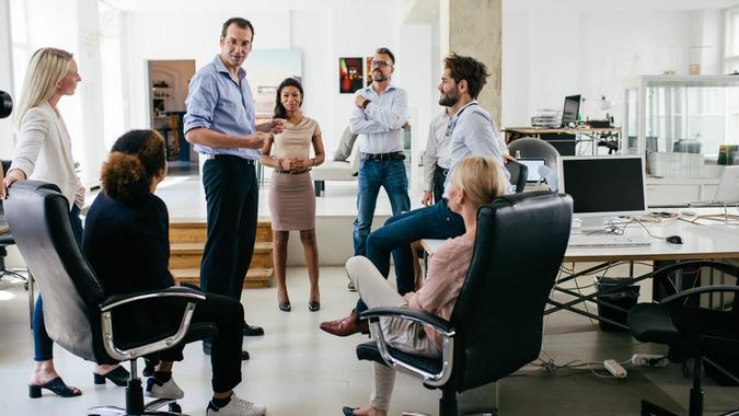 A group of colleagues in a circle are holding a meeting together in a bright, modern office space.