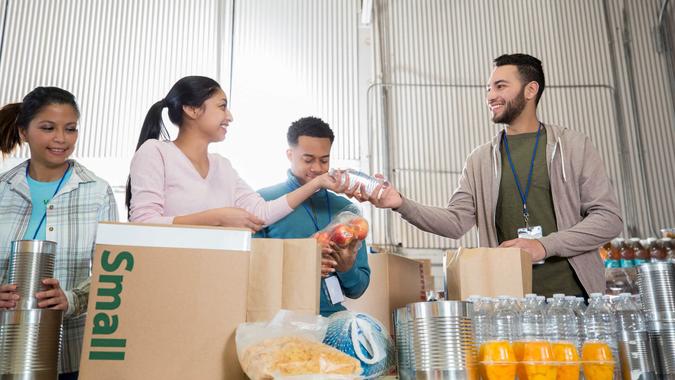 In this low angle view, a group of volunteers sorts food together on a table in a food bank warehouse.