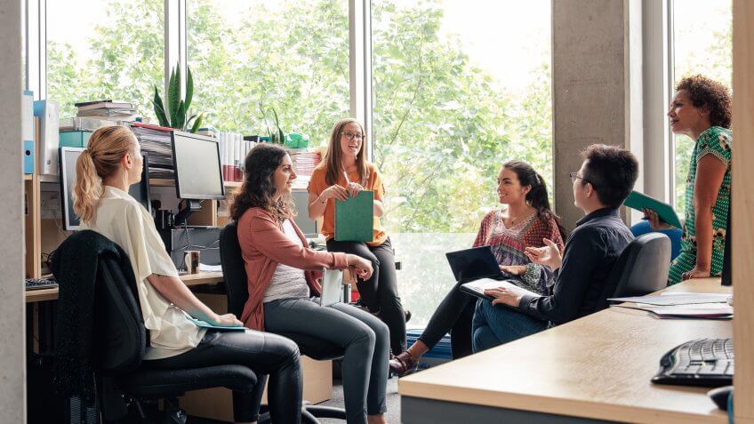 A group of science student graduates, are sitting casually around some desks together, having an informal discussion.
