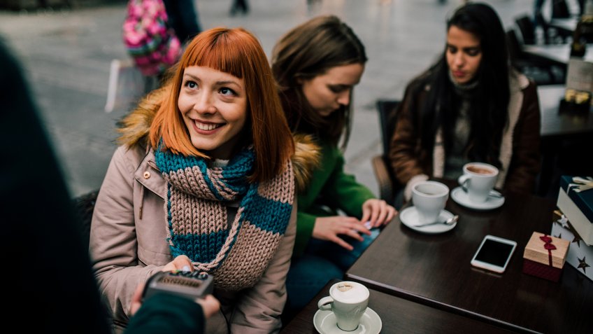 Happy young girl with red hair paying with credit card at coffee shop.