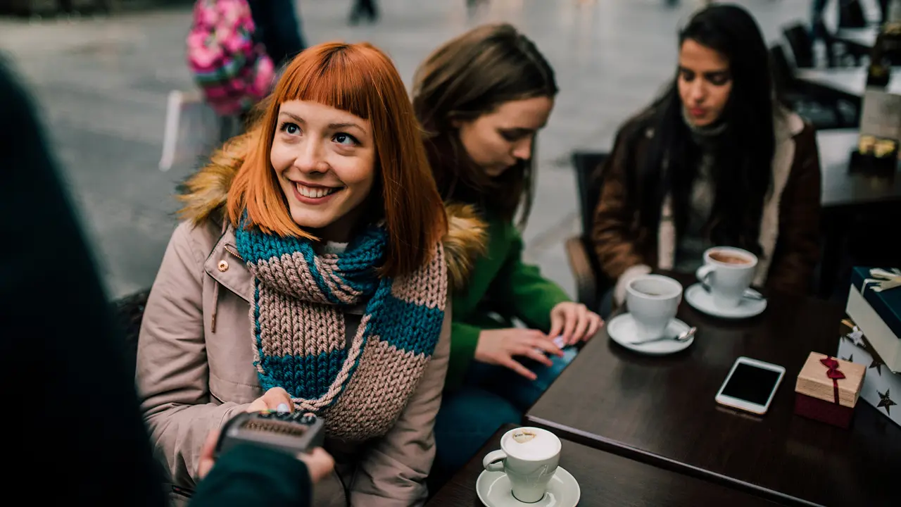 Happy young girl with red hair paying with credit card at coffee shop.