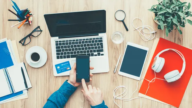 Man shopping online at home using a laptop and a credit card, he is making a mobile payment using his smartphone, top view.