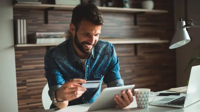 Man holding his credit card and doing online banking on his tablet.