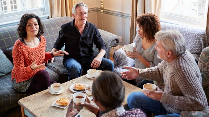 Group Of Middle Aged Friends Meeting Around Table In Coffee Shop.