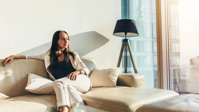 Portrait of successful businesswoman wearing elegant formal suit sitting on leather sofa relaxing after work at home.