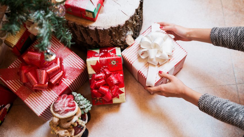 Close up of woman hands putting down a gift box under a Christmas tree.