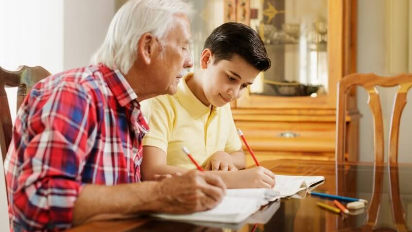 Happy little boy doing school homework with old man at home.