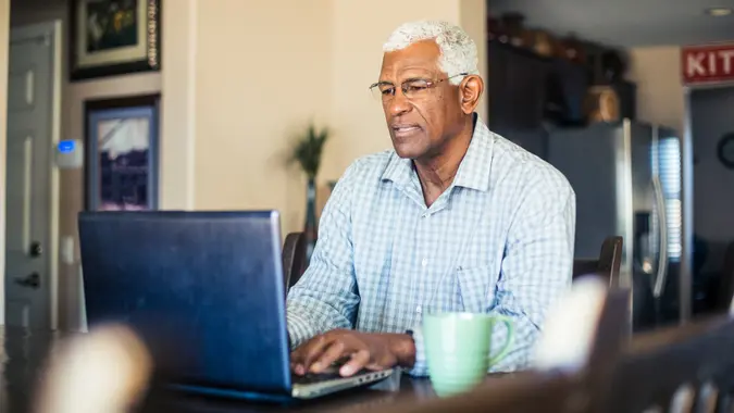 A senior black man works from his computer at home.