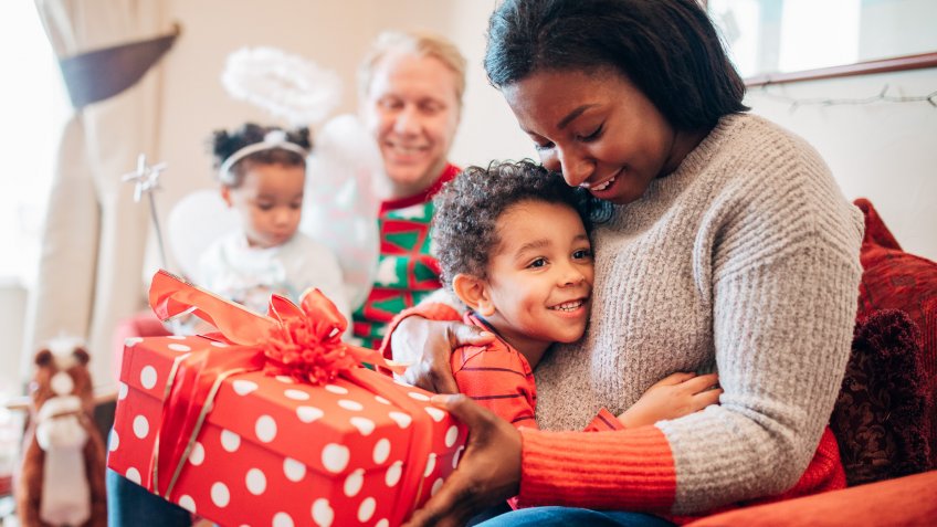 A little boy happily hugs his mother as she receives a gift from him on Christmas morning.