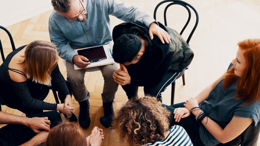 Supportive therapist comforting a young man who lost his parents in group therapy for people in mourning.