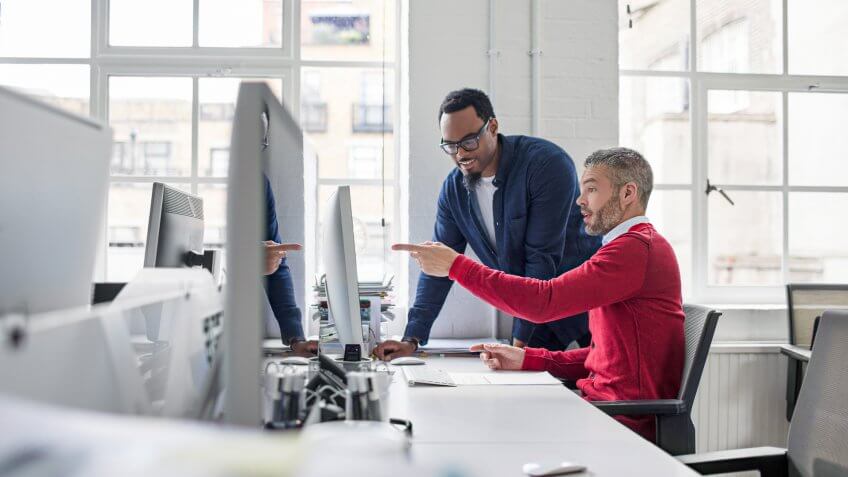 Mid adult businessman pointing at monitor to colleague.