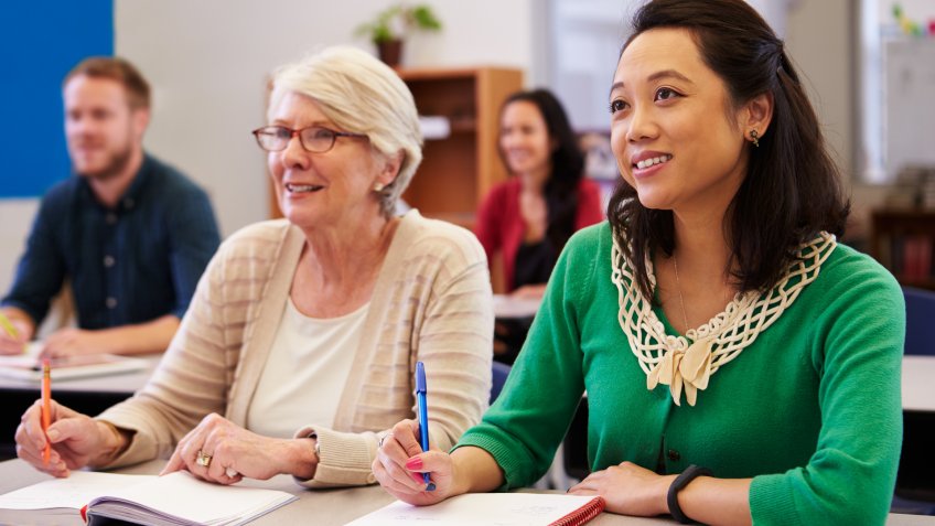 Two women sharing a desk at an adult education class look up.