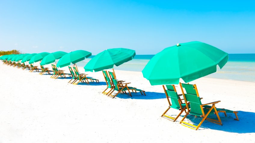 Green beach loungers and umbrellas at white sandy beach.