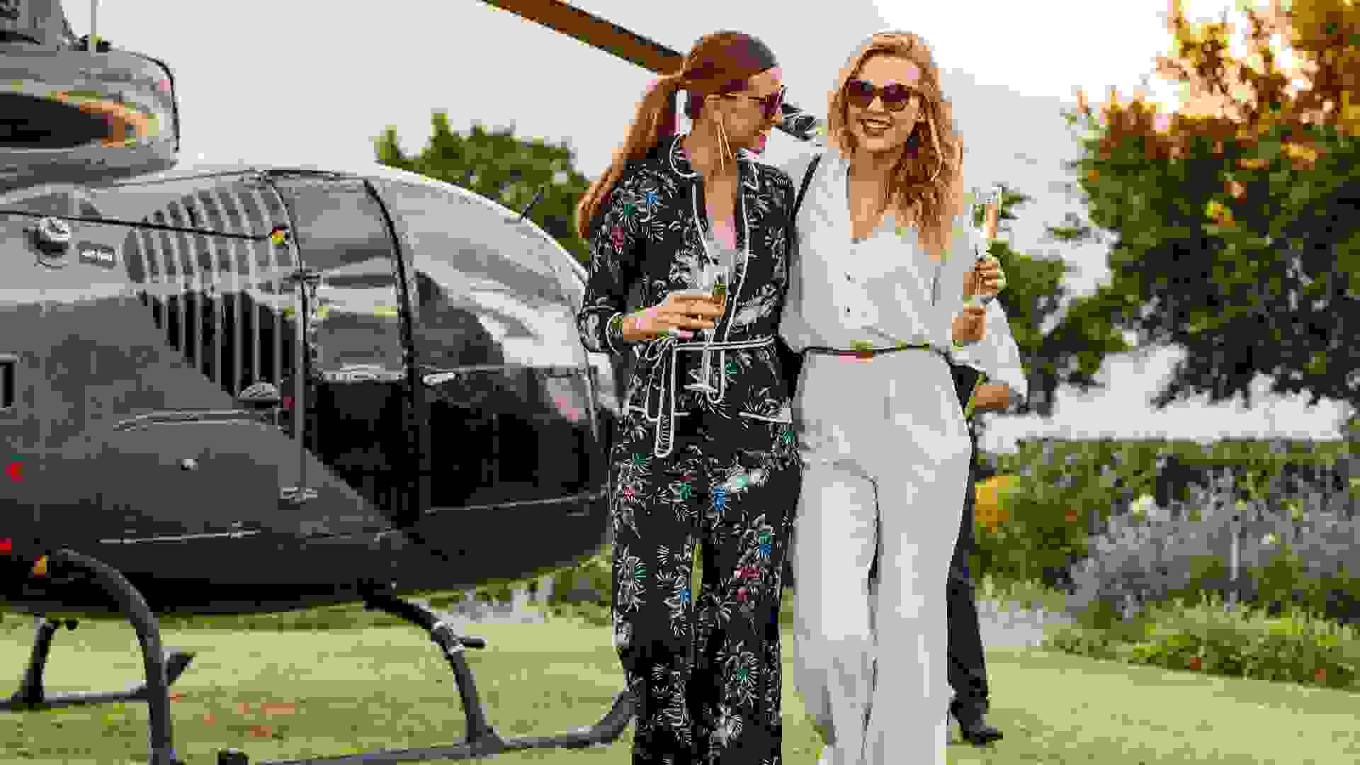 Two young women walking away from a helicopter with a glass of wine in their hands.