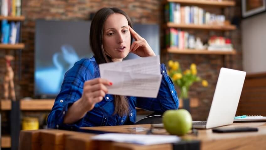 Woman is holding overdue bills before making online payment.