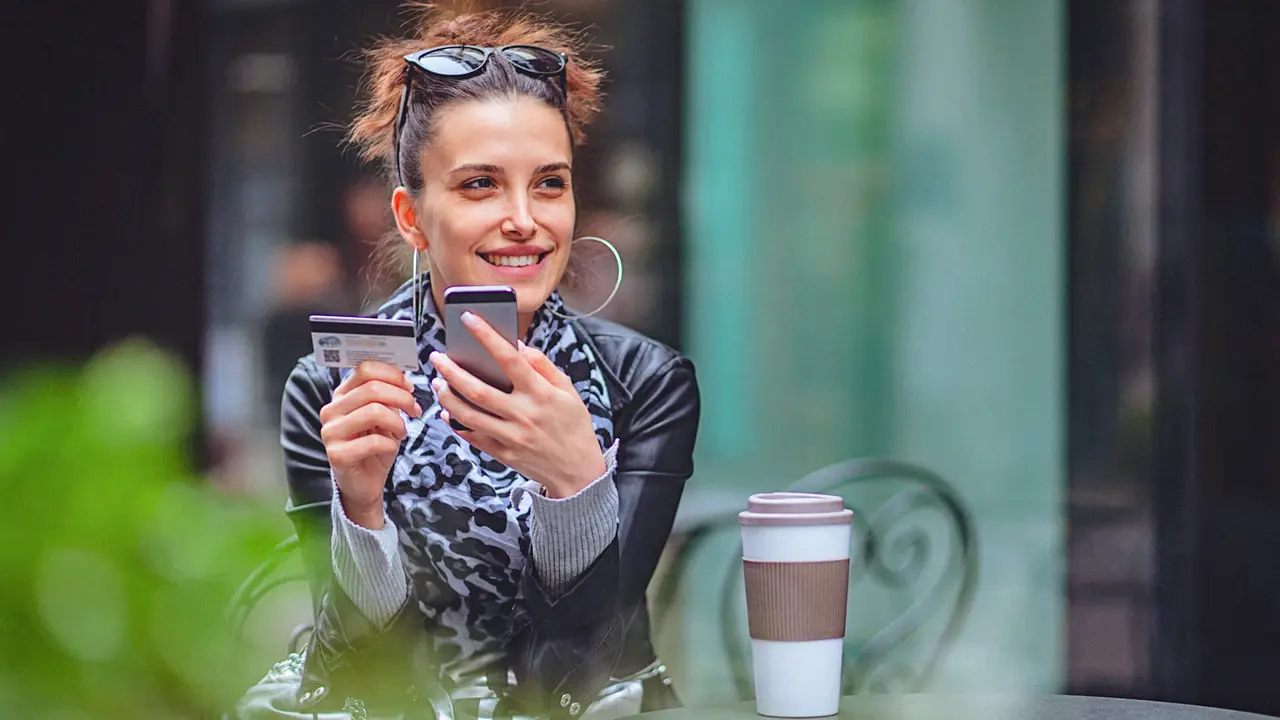 Close-up of a beautiful young woman in the city while using her credit card and a smartphone for an online transaction.