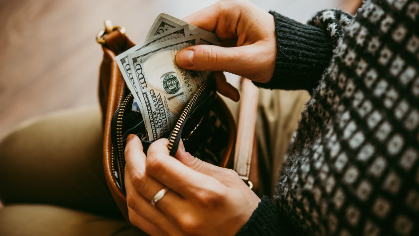 Girl's hands holding dollar bills, small money pouch and leather bag.