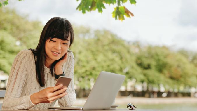 Shot of smiling young woman using mobile phone at outdoor cafe.