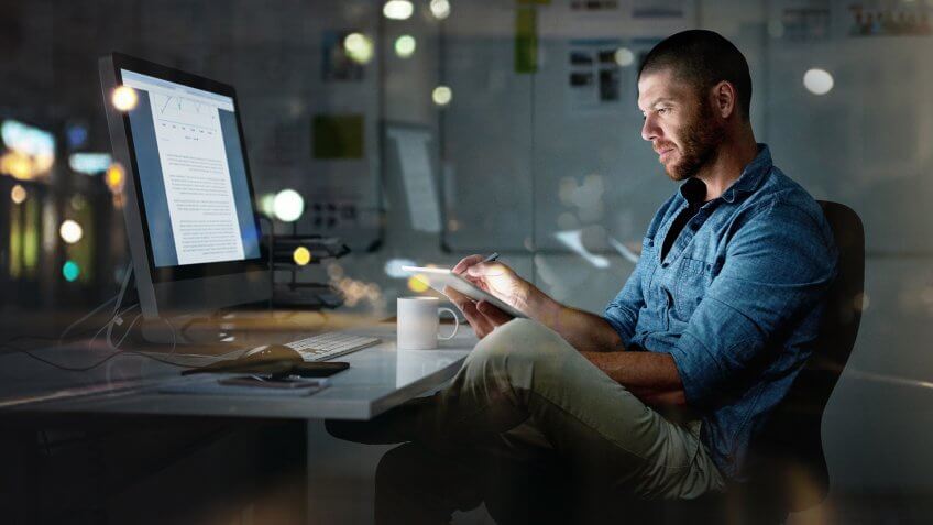 Shot of a businessman using a computer and digital tablet during a late night at the office.