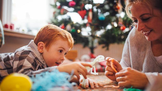 A young mother and her son are celebrating Christmas morning together, they are both lying on the floor and playing with newly opened toys together.
