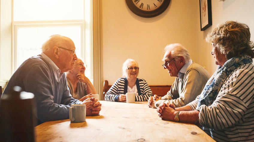 Group of senior people sitting together at a tablet at care home and sharing memories.