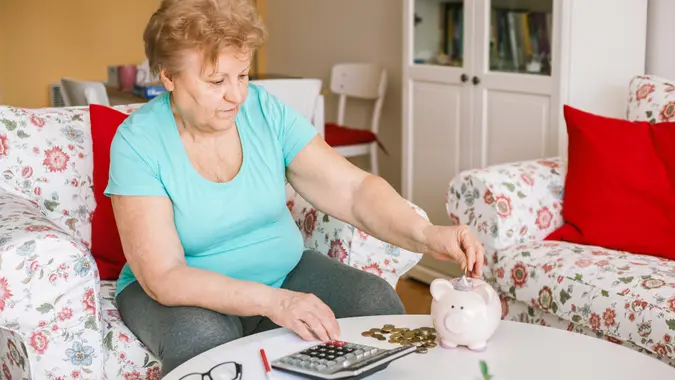 Mature 60s woman saving retirement money with a piggy bank at home.