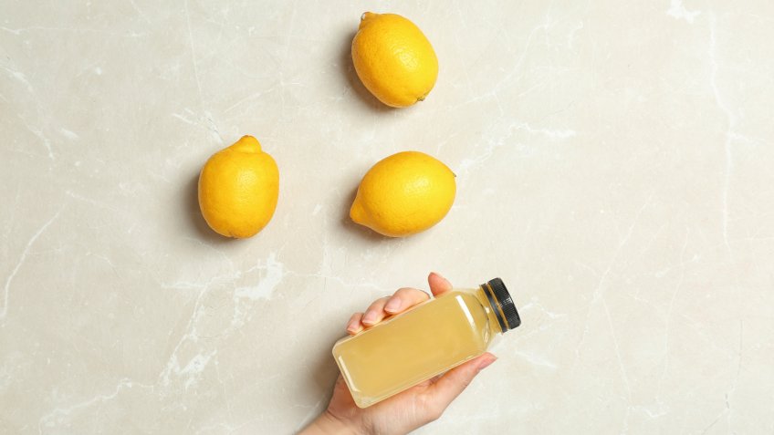 Woman holding bottle with fresh juice near lemons
