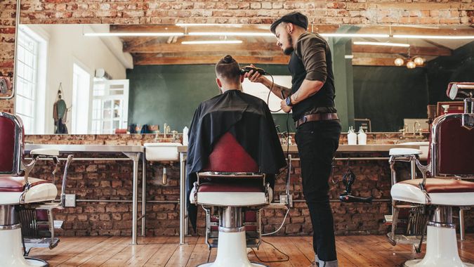  Vue arrière d'un beau coiffeur coupant les cheveux d'un client masculin.