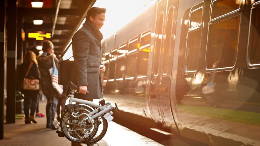 Businessman holding folding bicycle on railway platform about to board a train.