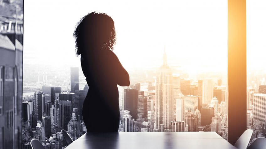 Silhouetted shot of a young businesswoman looking at a cityscape from an office window.