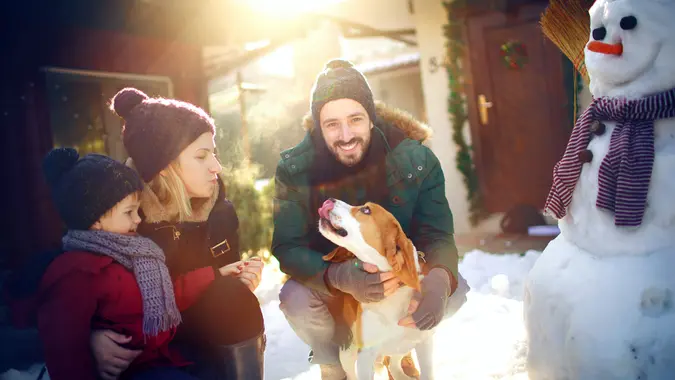 Smiling couple with a child and a dog enjoy outdoors on the snow .