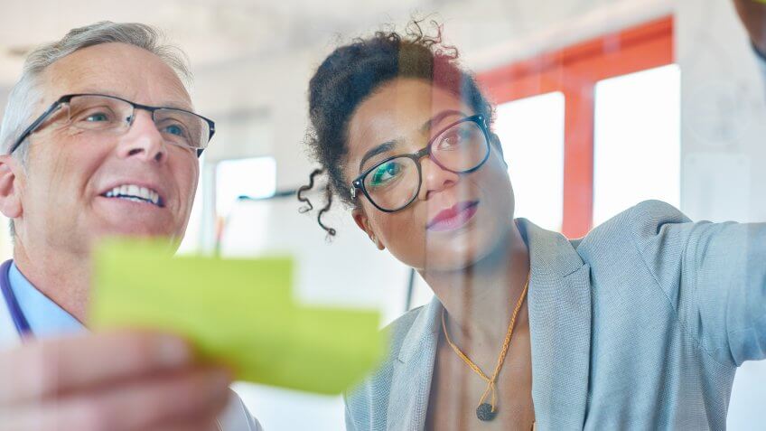 A saleswoman is presenting some ideas to a senior doctor on a glass interactive board .