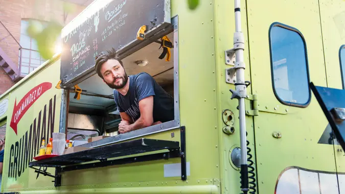 Adult man with beard waiting for clients in food truck in a city street on a bright summer day.