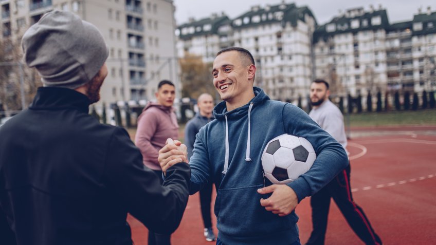 Group of men, playing soccer outdoors on the urban field, greeting before the game.