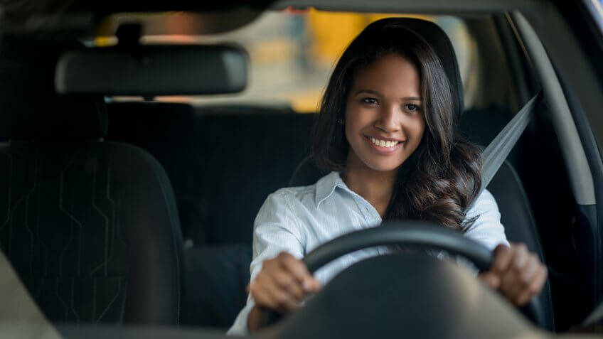 Happy African American woman driving a car at a dealersehip or an auto repair shop - lifestyle concepts.
