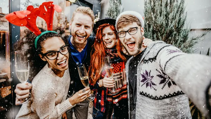 Group of smiling men and women taking selfie outdoors while snowing.