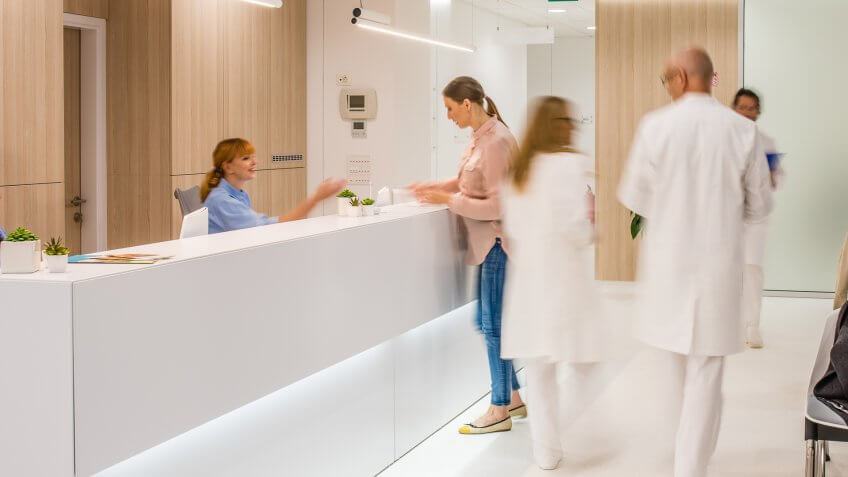 Blurred motion of doctors walking in clinic, patients sitting on chair.