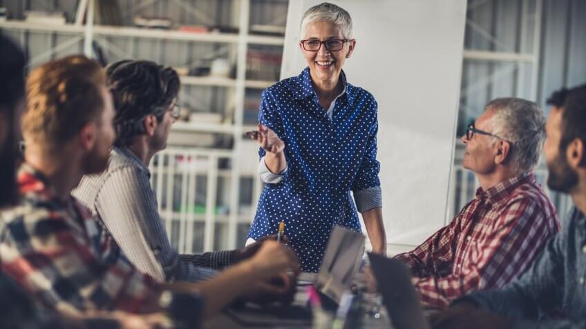 Happy mature businesswoman talking about new business plans with her male team in a board room.