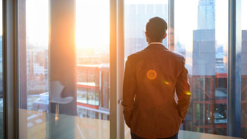 Male office worker looking at view through window of modern office over city.
