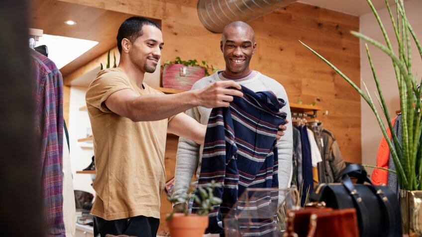 Two young men holding up clothes to look at in clothes shop.