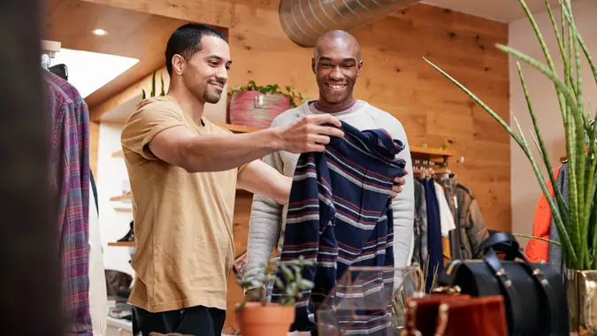 Two young men holding up clothes to look at in clothes shop.