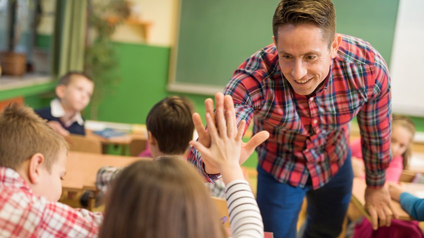 Smiling teacher giving high five to elementary student.