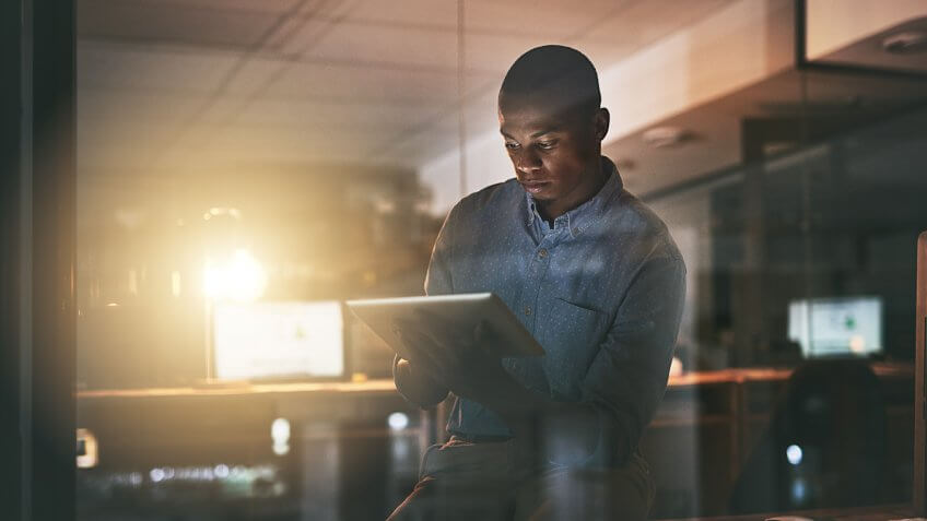 Shot of a young businessman using a digital tablet during a late night in a modern office.