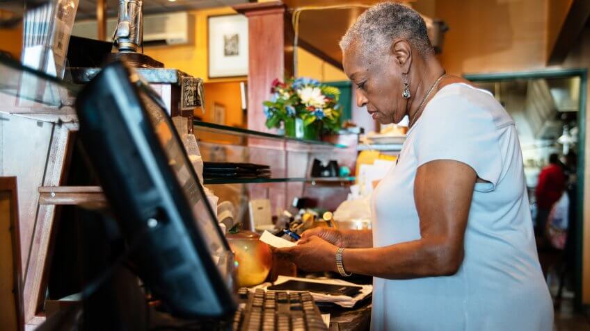 The senior Black woman working with the computerized cash register behind the counter in the small restaurant in New York State, USA.